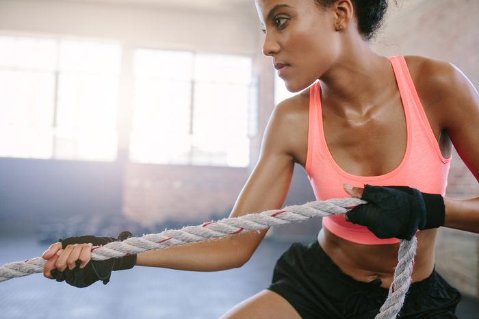 Close up shot of fit young woman exercising with rope at a gym. Strong african female pulling rope at gym.