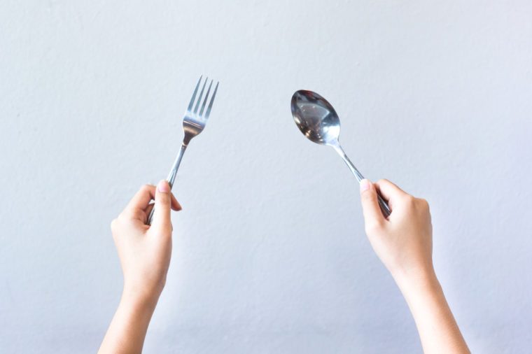 Woman hands isolated showing two hands holding spoon and fork on grey background, gesture of eating dinning.