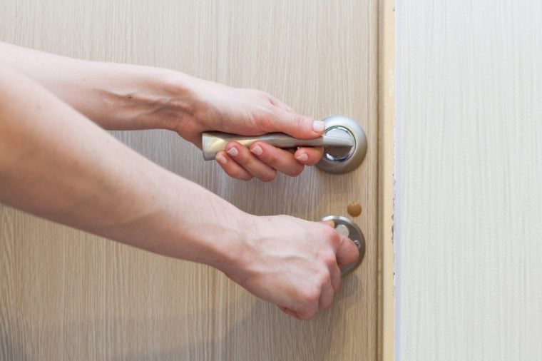 A hand trying to open the door by holding the doorknob with a white copy space on the door.