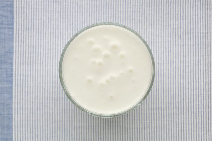 Yogurt or clean white smoothie glass top view on the blue textile background