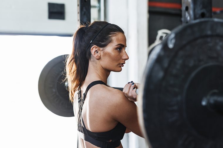Portrait of muscular young woman standing at gym with barbell