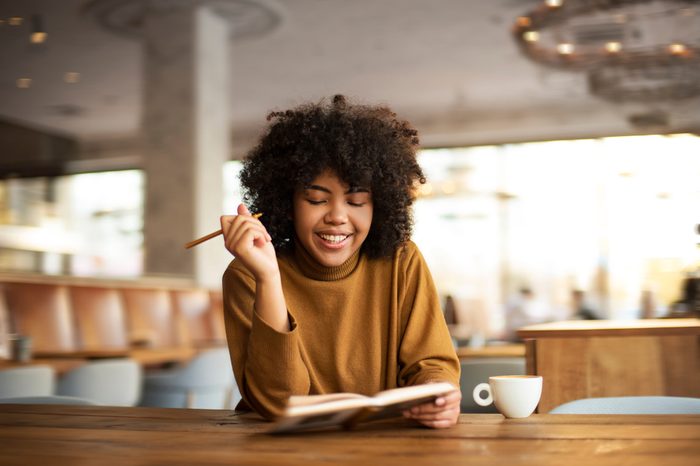 A young girl of African-American appearance sits at a table. She has a coffee break in a warm uninhabited atmosphere. She talks on the phone with her friends, has a rest and drinks tasty coffee