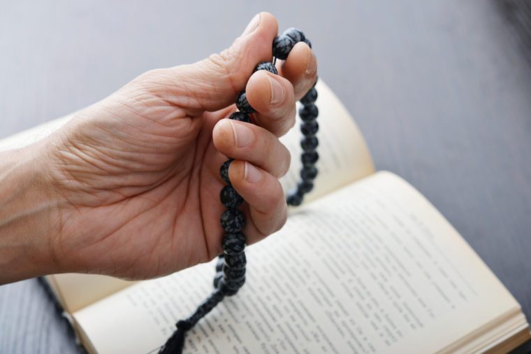 Male hand holding rosary beads closeup and koran on background.