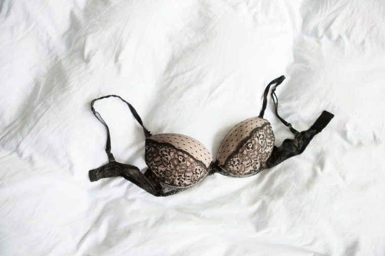 Black lace bra lying down on the white bed sheets.