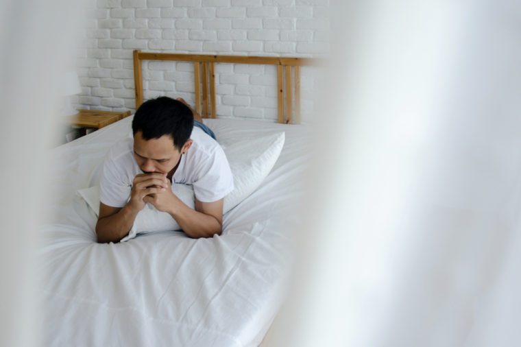 Men are sitting at the edge of the bed in the room and have stress.Young man wearing a white shirt with both hands on his head. Because of pain.Do not focus on objects.