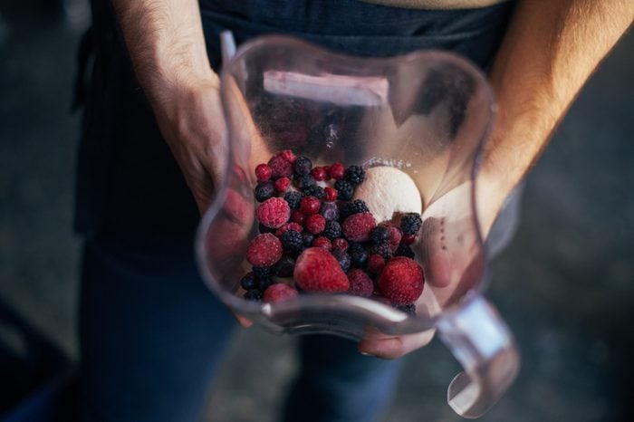 Soft focus of man holds blender or food processor with frozen forest berries, organic bananas and ice cream. Preparation recipe for smoothie or healthy blended drink for fitness diet