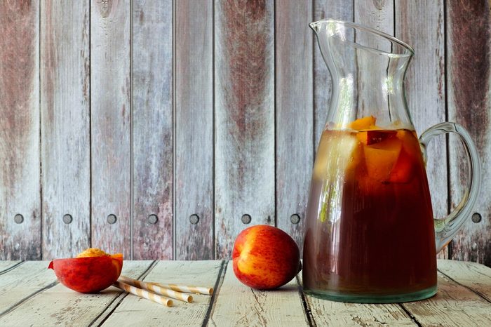 Pitcher of peach iced tea with fruit slices against a rustic wooden background