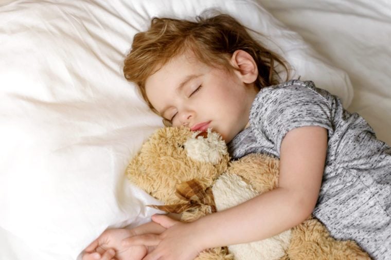 Beautiful baby girl sleeping in my own bed at home with a favorite toy bear.