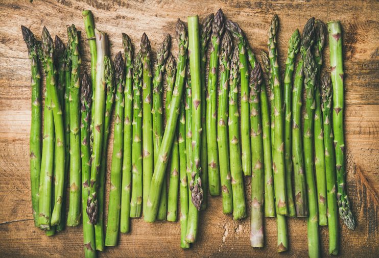 Seasonal harvest produce . Flat-lay of raw uncooked green asparagus in row over rustic wooden background, top view. Local market food concept