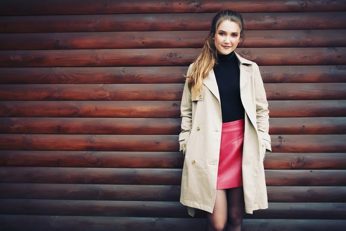Beautiful young model with ponytail wearing black turtleneck, red leather skirt and trench coat. Professional make-up, hair style and styling. Autumn woman portrait in fall outdoors