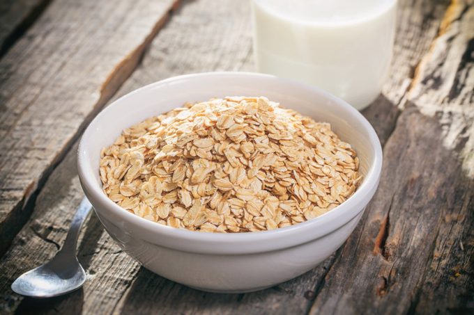 Bowl of oat flakes and glass of milk, on wooden surface.