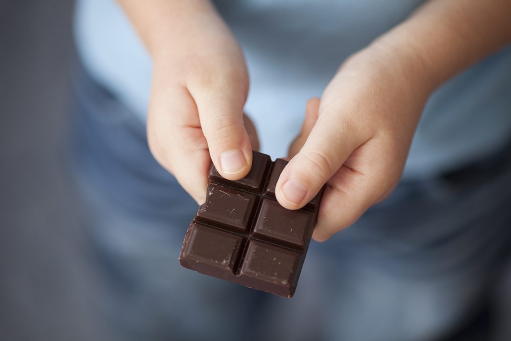 Broken piece of dark chocolate in child's hands.