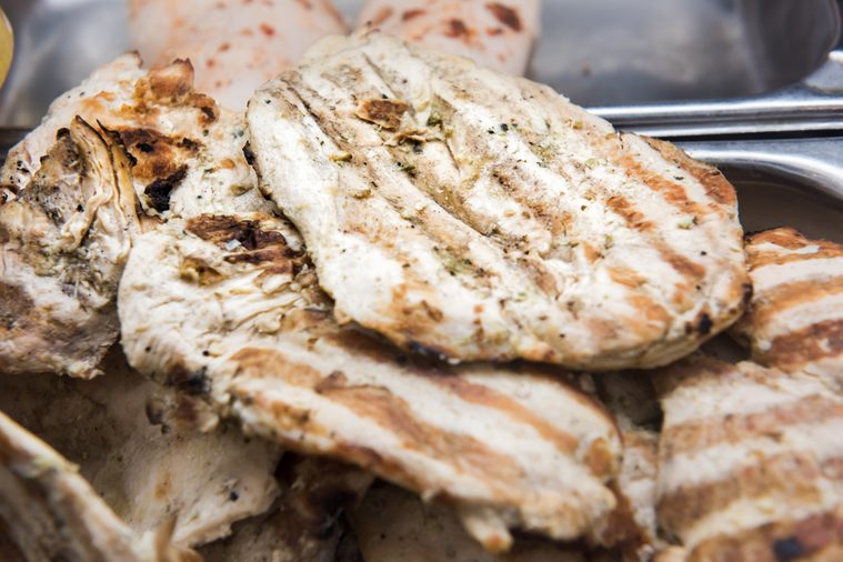 Closeup of grilled white chicken breasts cutlets white meat pile stack on display in restaurant food counter buffet commercial kitchen