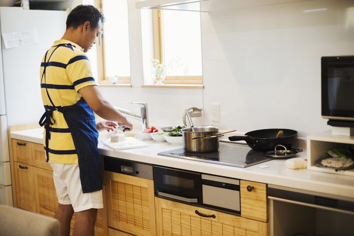 MODEL RELEASED Family home. A man in a blue apron preparing a meal with his son.