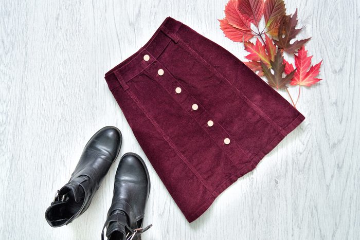 Burgundy suede skirt, black boots and red leaves. Fashionable concept.