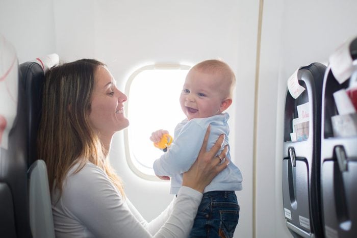 Young mom, playing and breastfeeding her toddler boy on board of aircraft, going on holiday