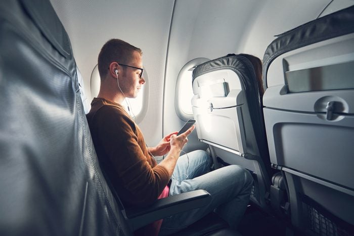 Connection in the airplane. Young man (traveler) using smart phone during flight and listening music.