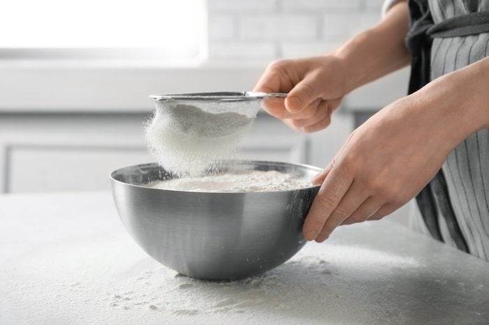 Woman sifting flour into bowl on table