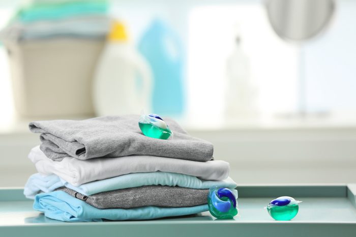 Stack of clothes and laundry pods on table at home