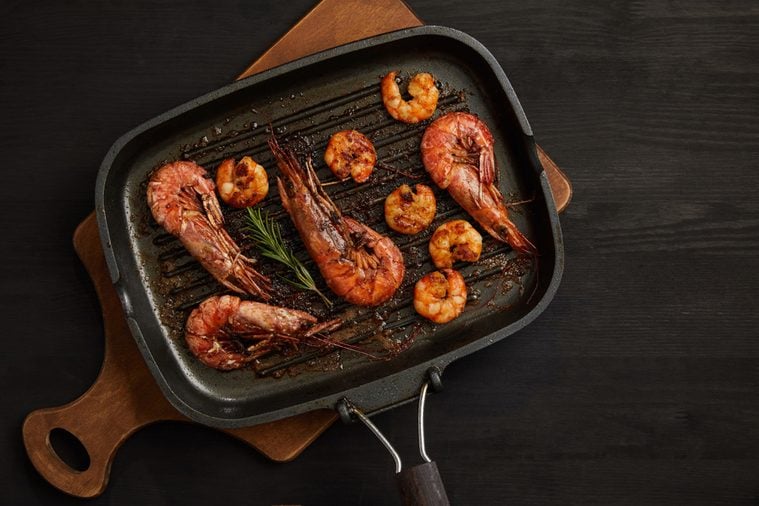 top view of grilled shrimps with rosemary on wooden cutting board on black tabletop