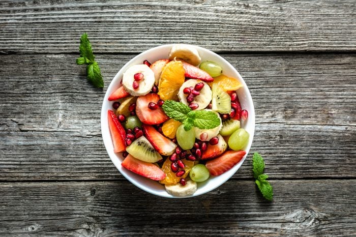 Fresh fruit salad, top view in a bowl on wooden background, vegetarian food concept