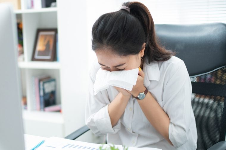 Women are sneezing and are cold. She is in the office.