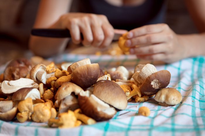 Woman cleaning wild mushrooms in the kitchen, porcini and chanterelles in the front