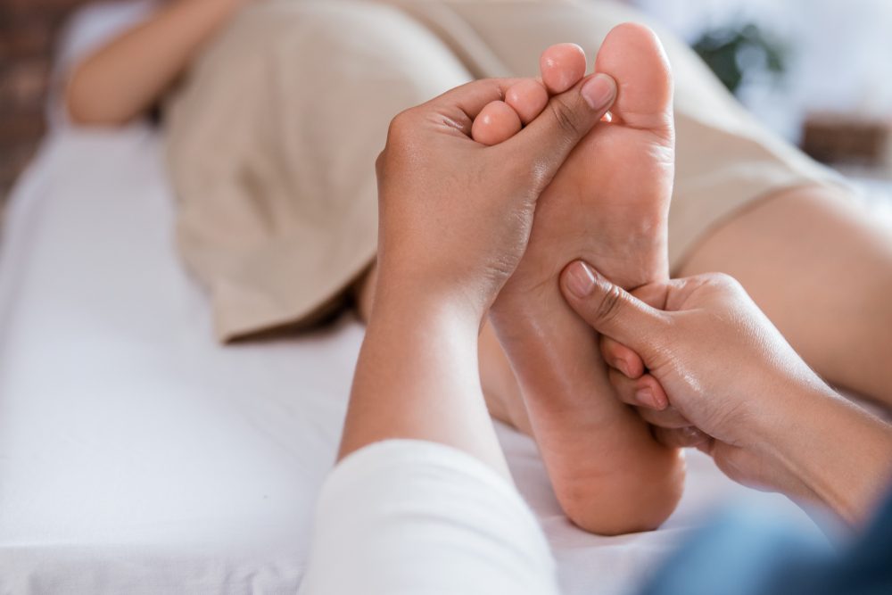 portrait of therapist giving relaxing reflexology Thai leg massage treatment to a woman in spa