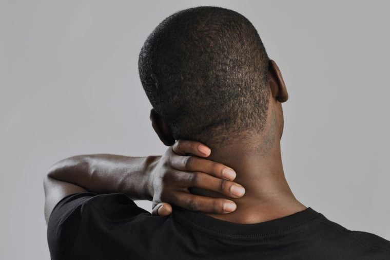Closeup of man rubbing his neck with hand as he aches with pain in the neck on grey background