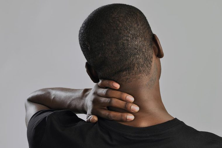 Closeup of man rubbing his neck with hand as he aches with pain in the neck on grey background