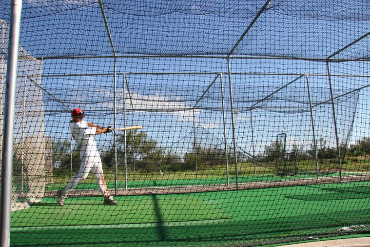 practicing hitting baseball in a batting cage