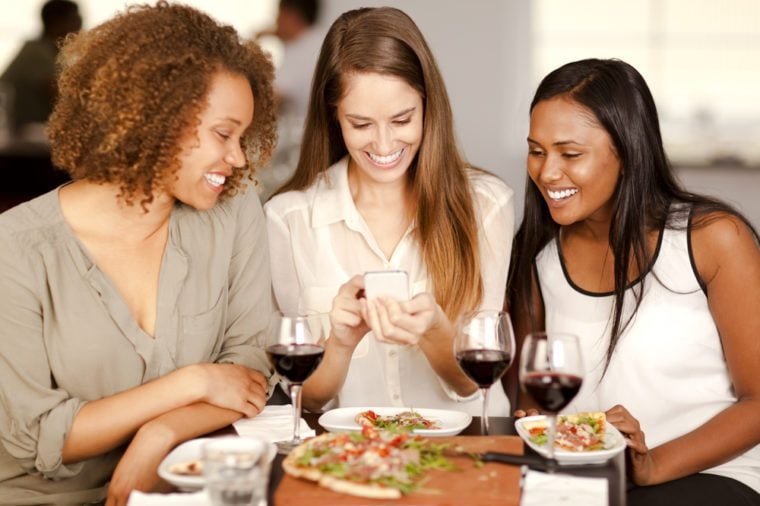 Group of mixed-race girls looking at a smartphone in a restaurant.