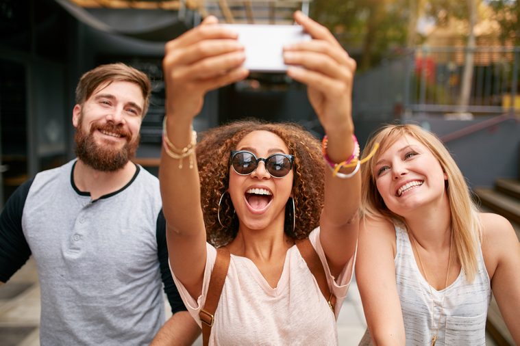 Group of smiling friends taking selfie with mobile phone. Multiracial man and women enjoying themselves outdoors and taking pictures with smart phone.