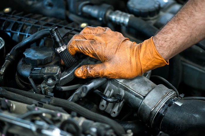 Hand of a mechanic in an oil covered glove resting on a car engine in a close up view conceptual of maintenance in a workshop, or of a career as a mechanic