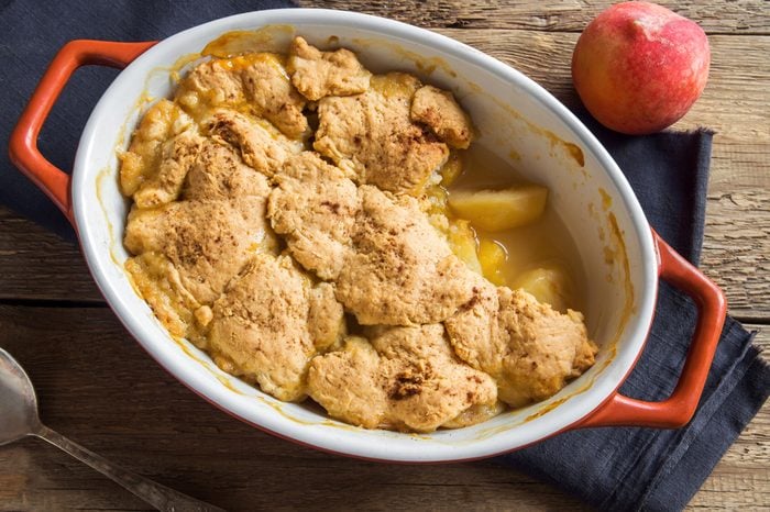 Homemade peach cobbler (crumble) in baking dish over rustic wooden background