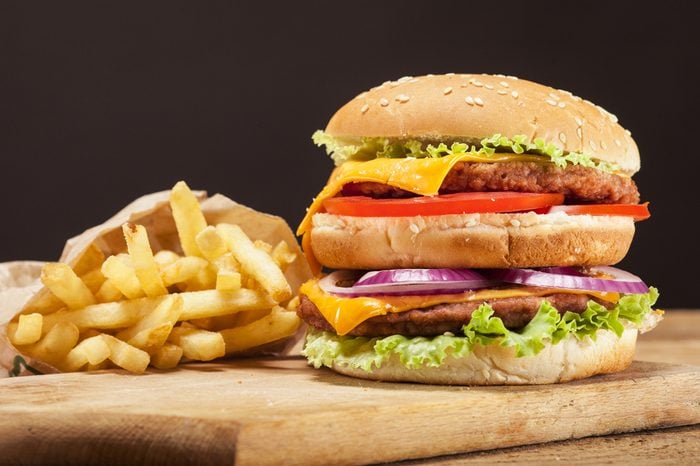 Fresh delicious double burger with cheese, tomato, onion, french fries and lettuce on wooden table and brown background with copy space