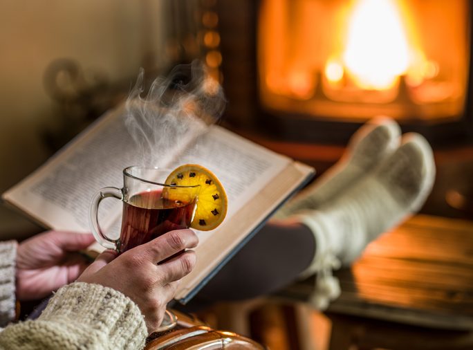 Hot mulled wine and book in woman hands. Relaxing in front of burning fire in the cold winter day.