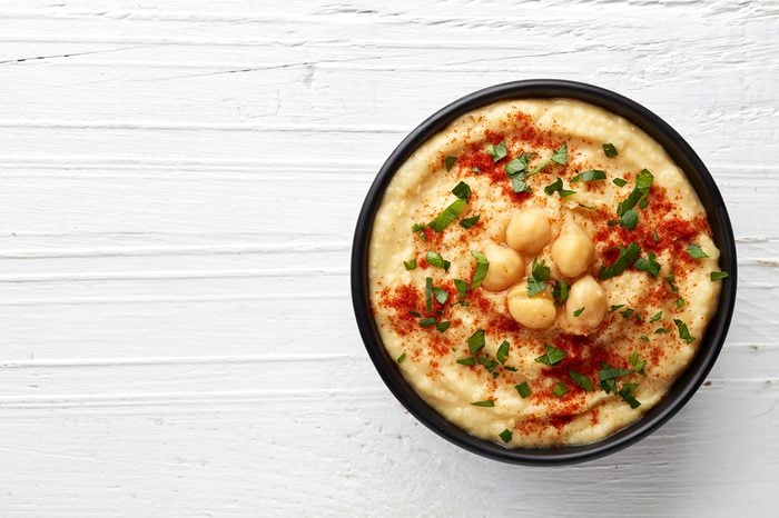 Bowl of homemade hummus on white wooden background from top view