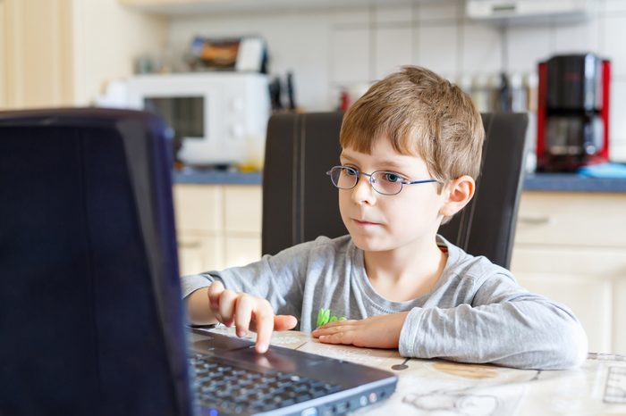 Little school kid boy with glasses playing game and surfing internet on computer. Child having fun with learning on pc. Education concept.