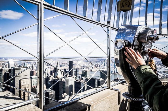 Close up of a girl that looks manhattan by telescope, from the Empire State Building