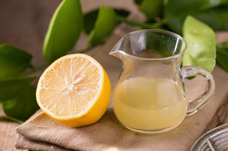 glass bowl of freshly squeezed lemon juice, lemon squeezer and ripe lemons on wooden background.