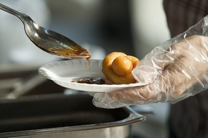 Catering dish up food, Chinese dumplings with sauce. Paper dish with dumpling in one hand and spoon with sauce in another hand.