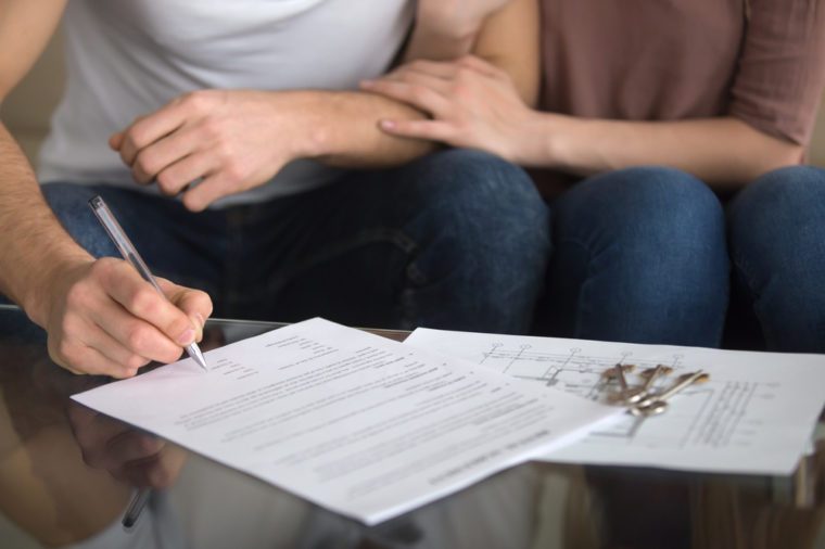 Buying and renting new home concept. Close up of loving couple signing rental agreement or sale purchase contract sitting on couch indoors, starting family life, approved loan to buy real estate 