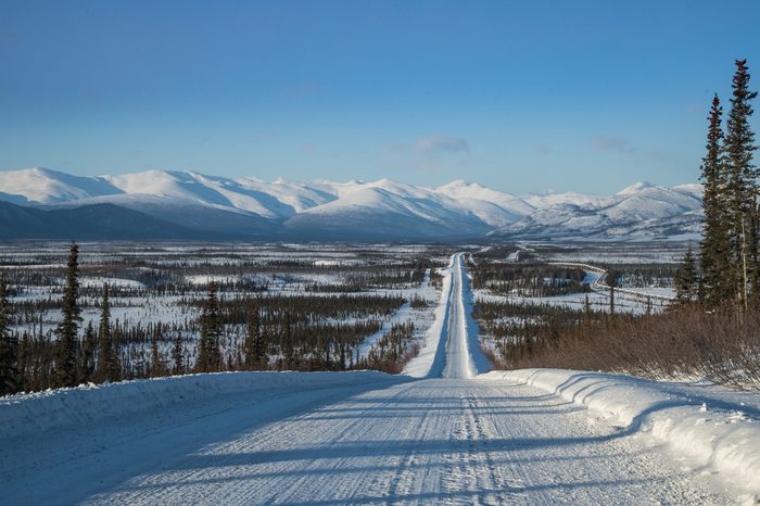view along dalton highway toward brooks range in north alaska in winter, with oil pipeline seen to right
