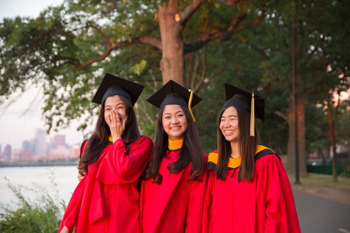 Group of Asian Female Graduates in Red Graduation Gowns Standing by Charles River at Sunset