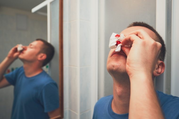 Man with nose bleed in bathroom. For themes of illness, injury or violence.