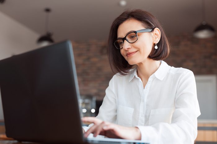 Adult elegant businesswoman in white shirt and glasses sitting with laptop in cafe. 