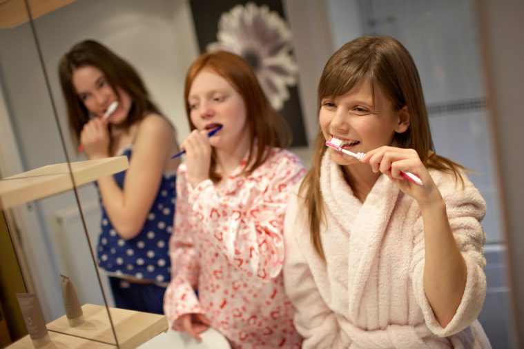Teenage girls brushing teeth