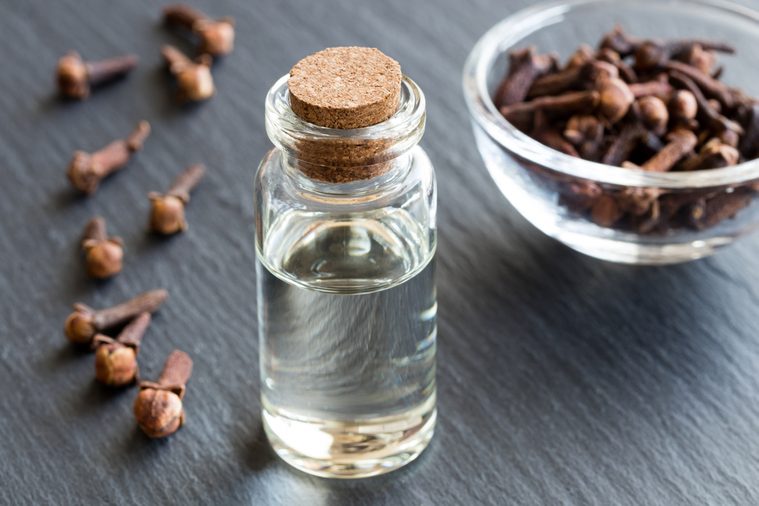 A bottle of clove essential oil with dried cloves in the background