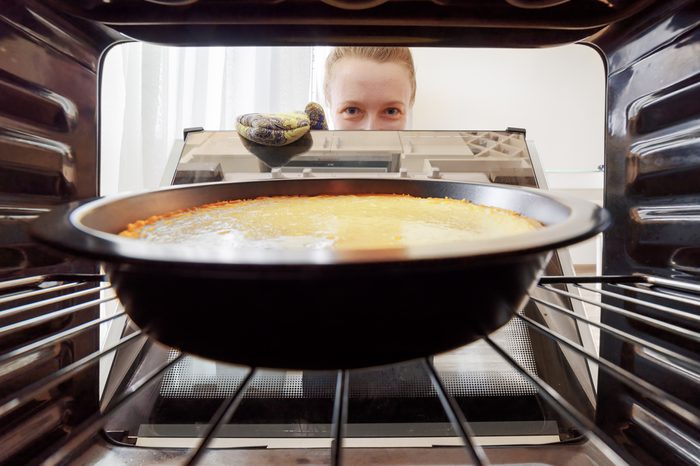 Young housewife looking at cheesecake into oven in kitchen. View from inside of the oven. Woman holding the oven door.